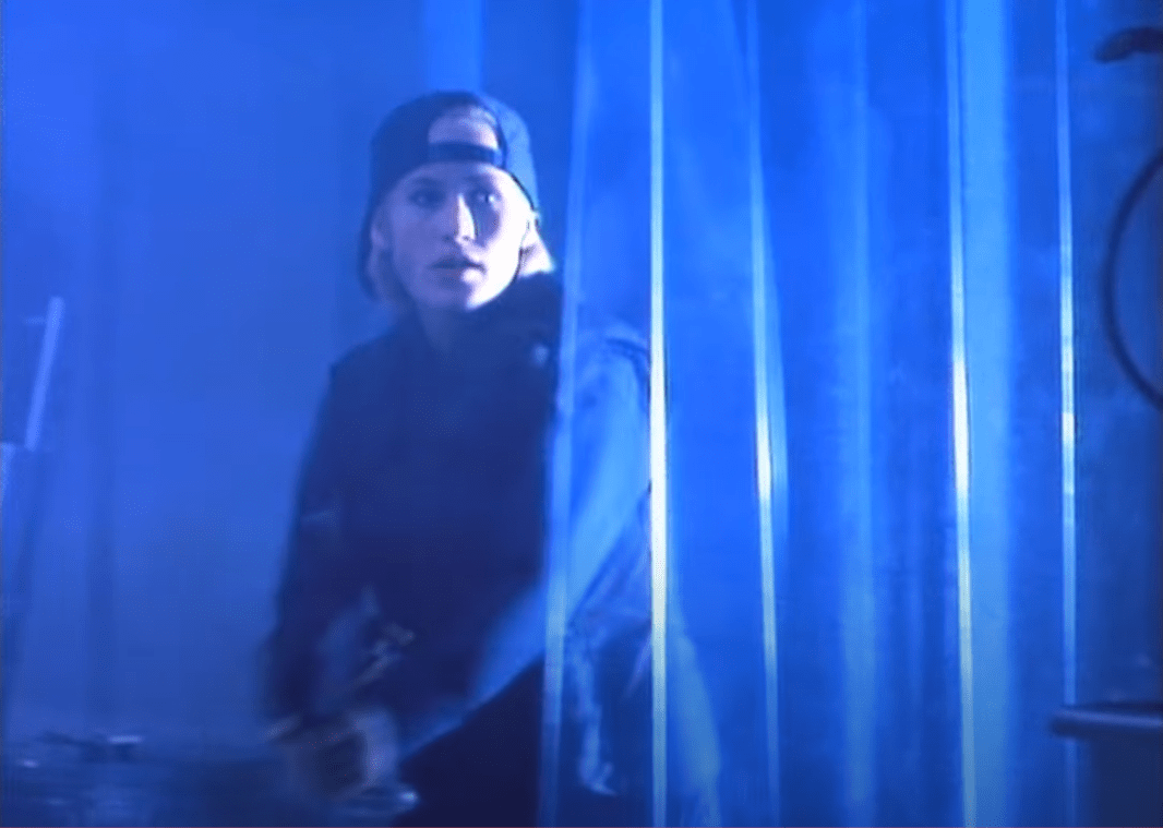 A picture of Casey coming into the drug camper to save Griffin's butt. She's wearing a backwards baseball cap and wielding a semi-automatic rifle.